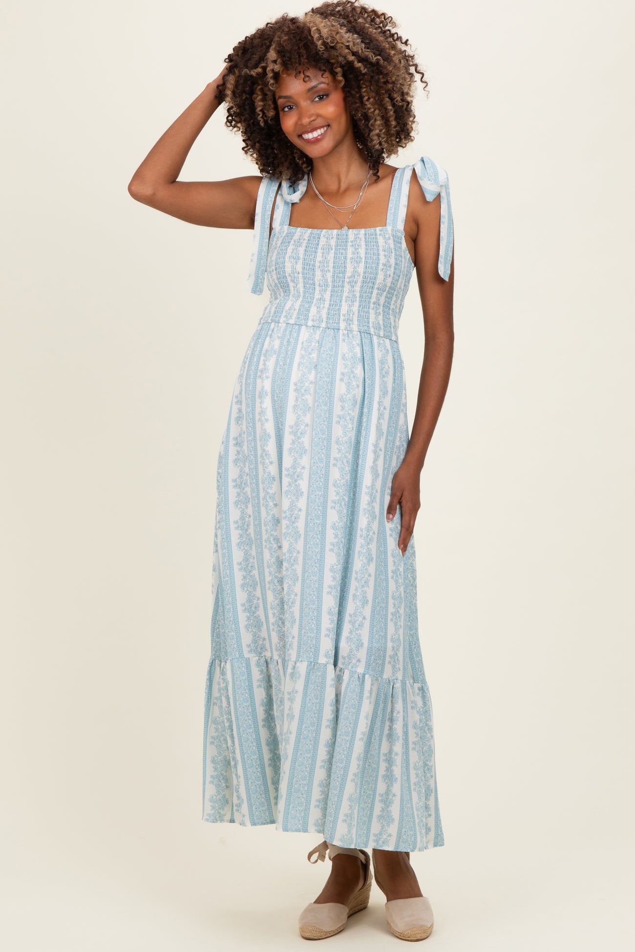 woman wearing a light blue floral maternity maxi dress with shoulder ties and smocked bodice, gently highlighting her baby bump