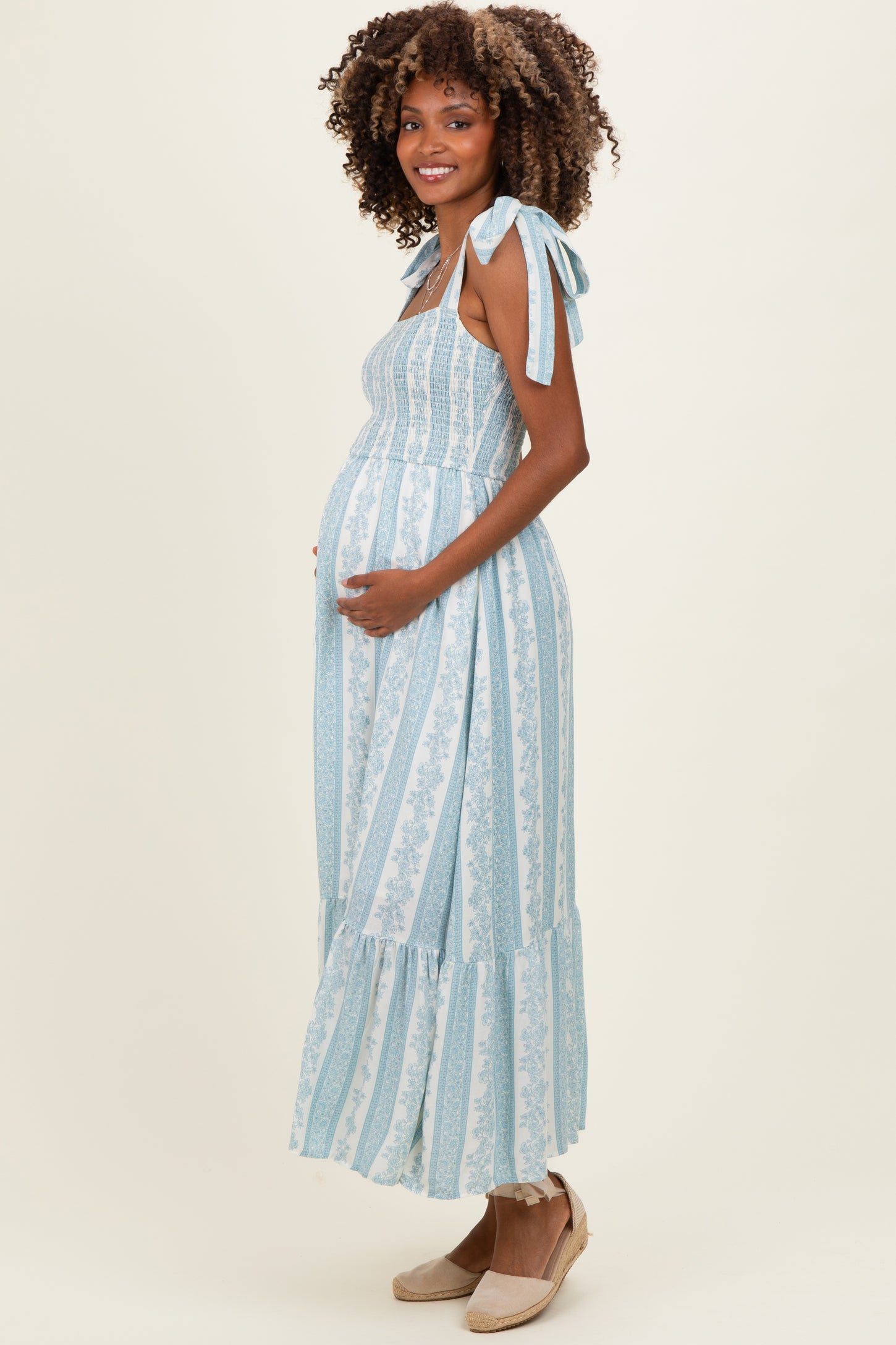 woman wearing a light blue maternity dress with tie straps and a ruffled hem, showcasing her baby bump