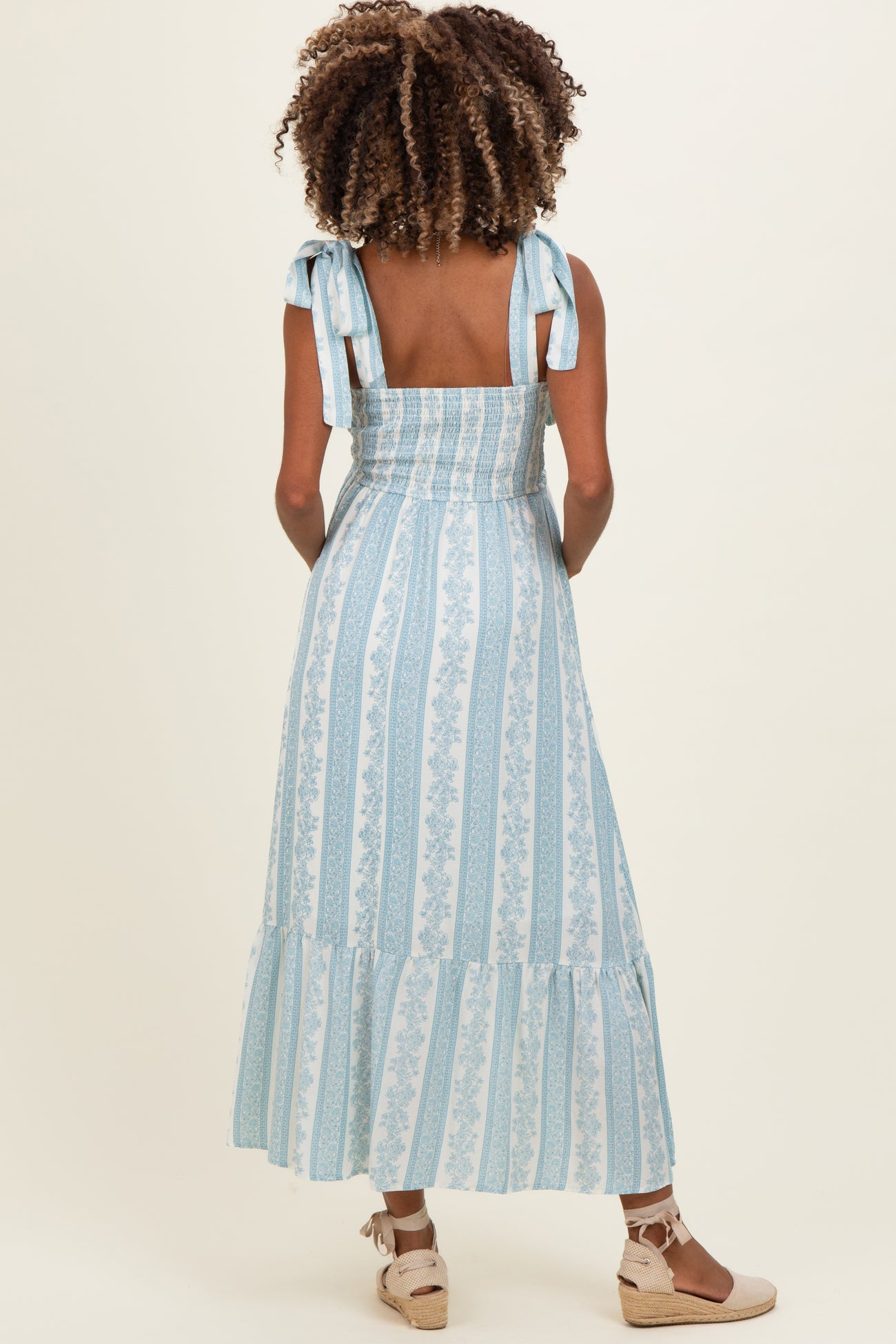 woman wearing a light blue patterned maternity dress with tie straps and a flowy skirt, showcasing her baby bump