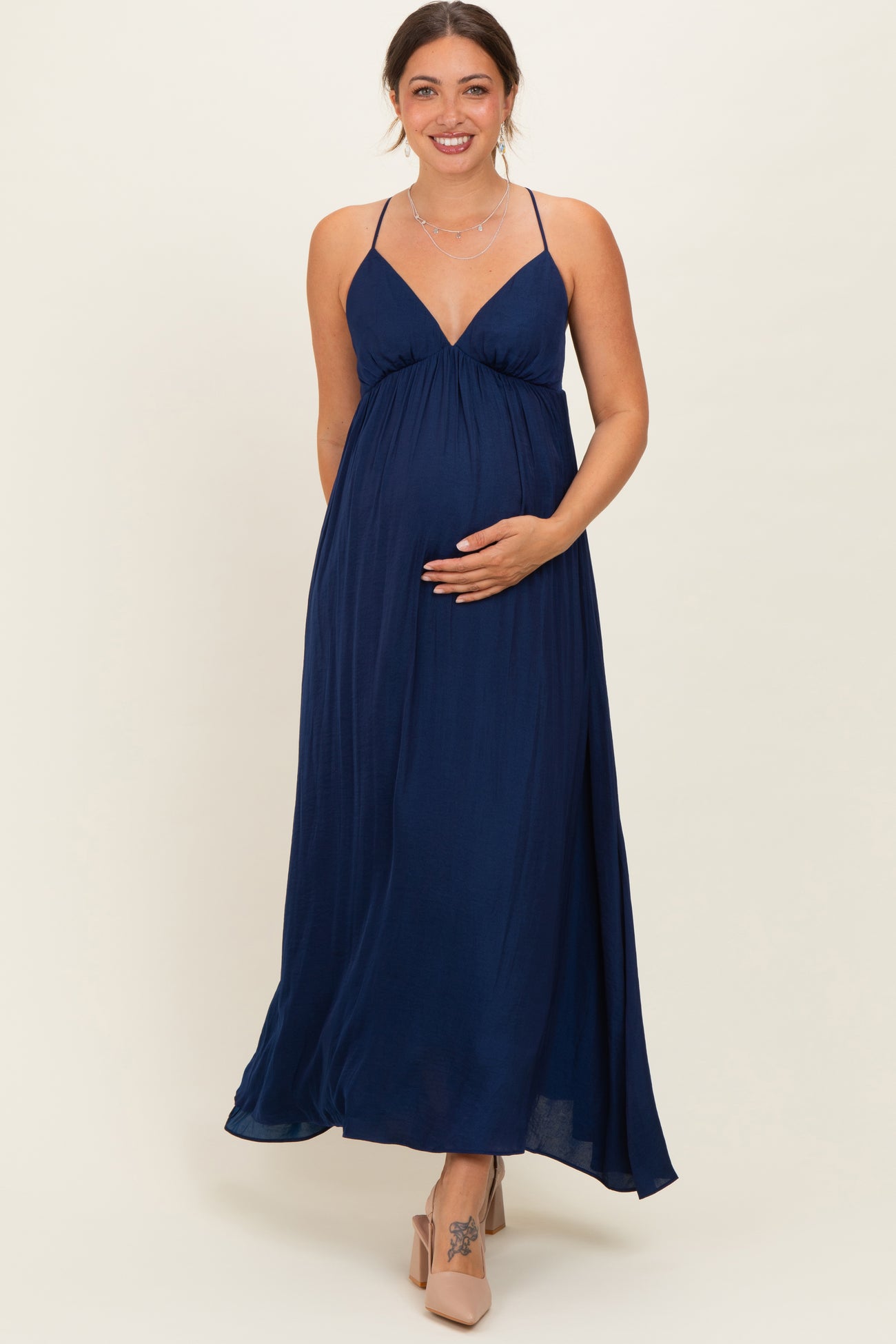 woman wearing a navy blue maternity maxi dress with a v-neck and adjustable straps, gently holding her baby bump