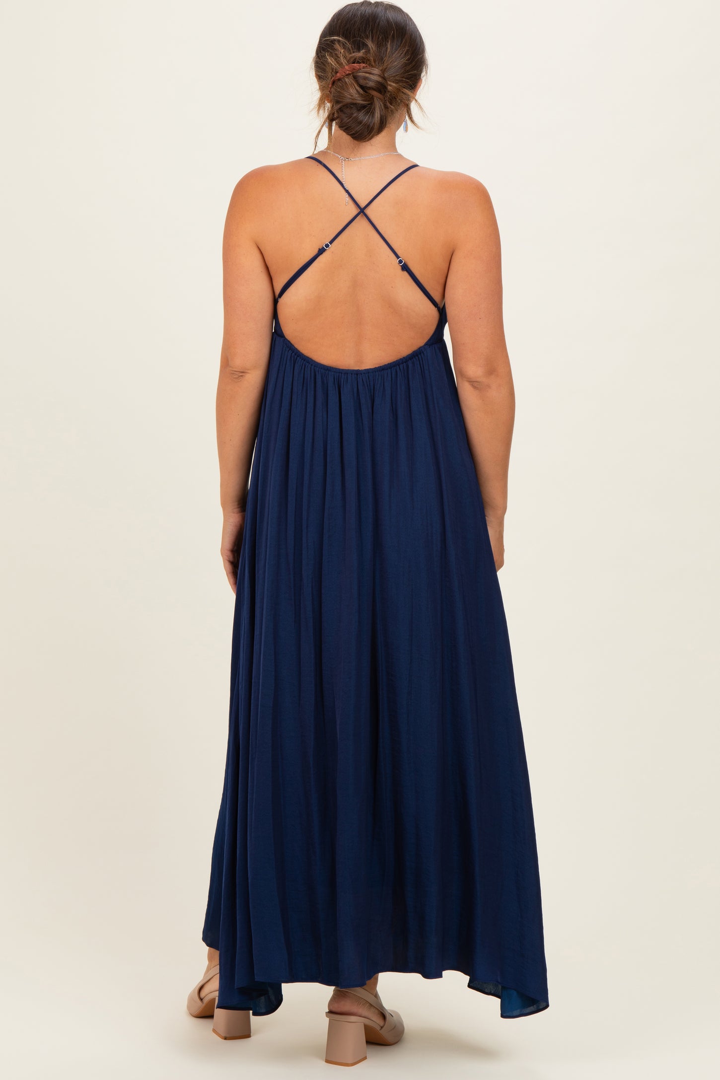 woman wearing a navy blue maternity maxi dress with crisscross straps and a flowing skirt, showing her baby bump