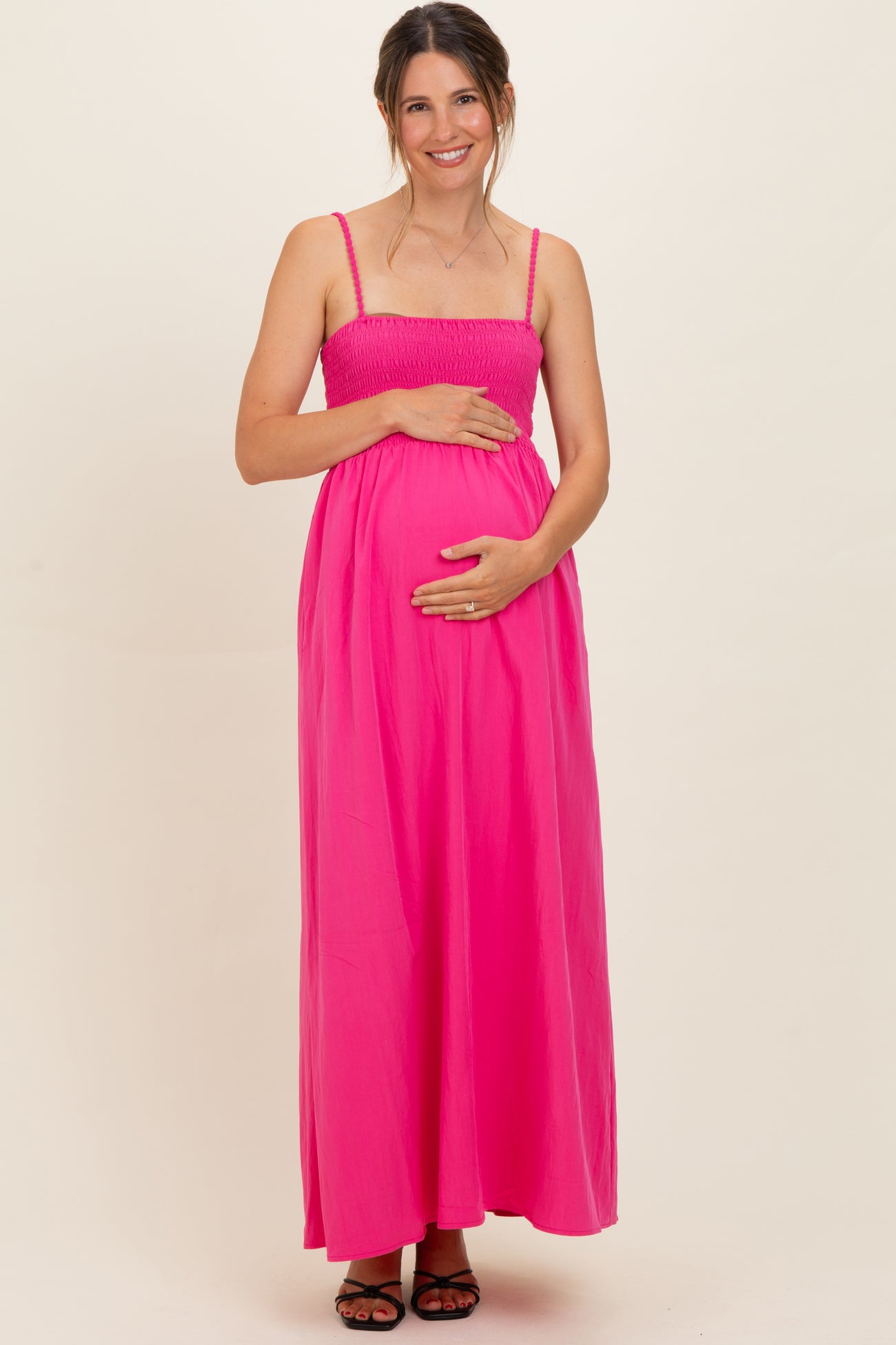 woman wearing a bright pink maternity maxi dress with smocked bodice and holding her baby bump