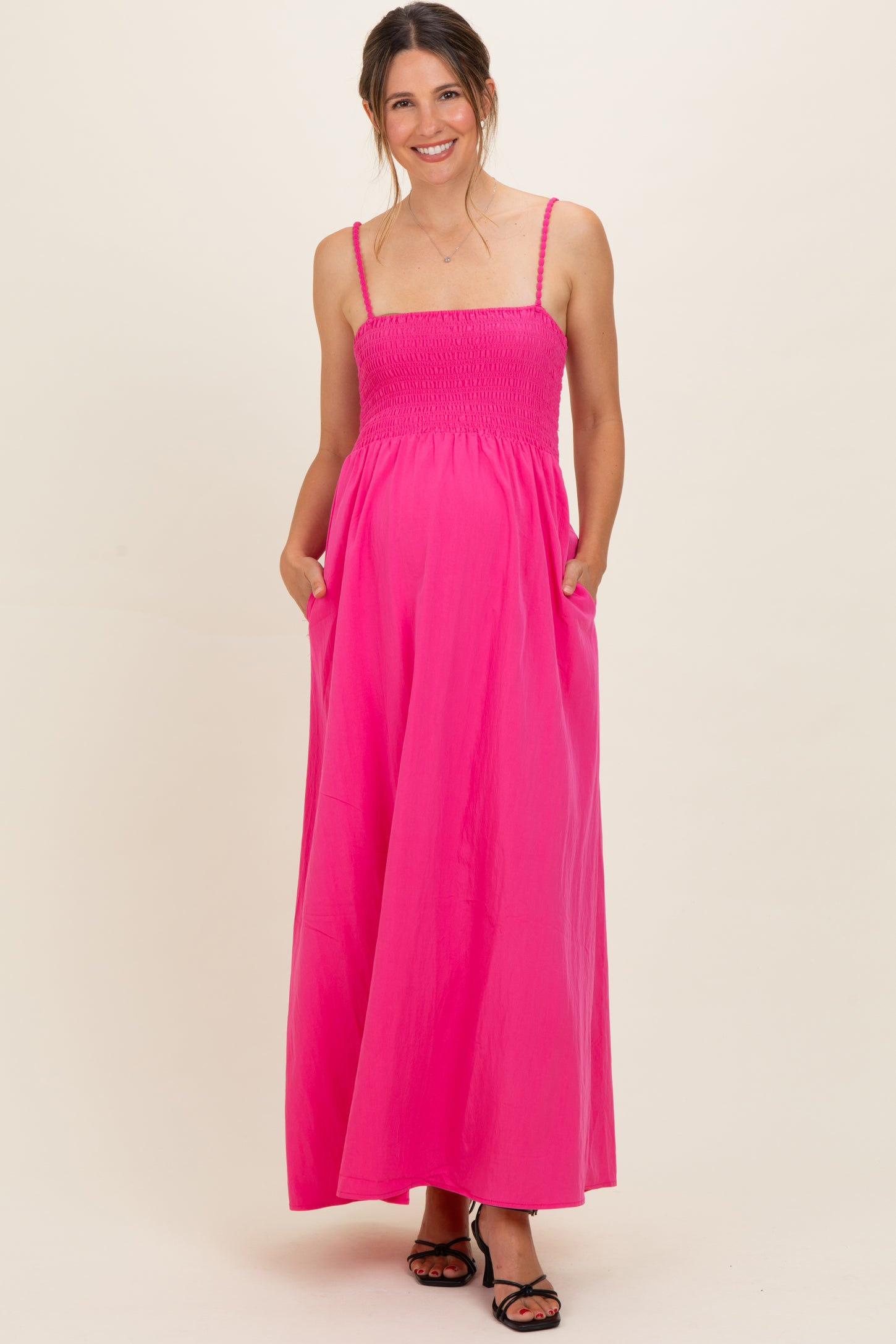 woman wearing a vibrant pink maternity maxi dress with smocked bodice and pockets, displaying her baby bump