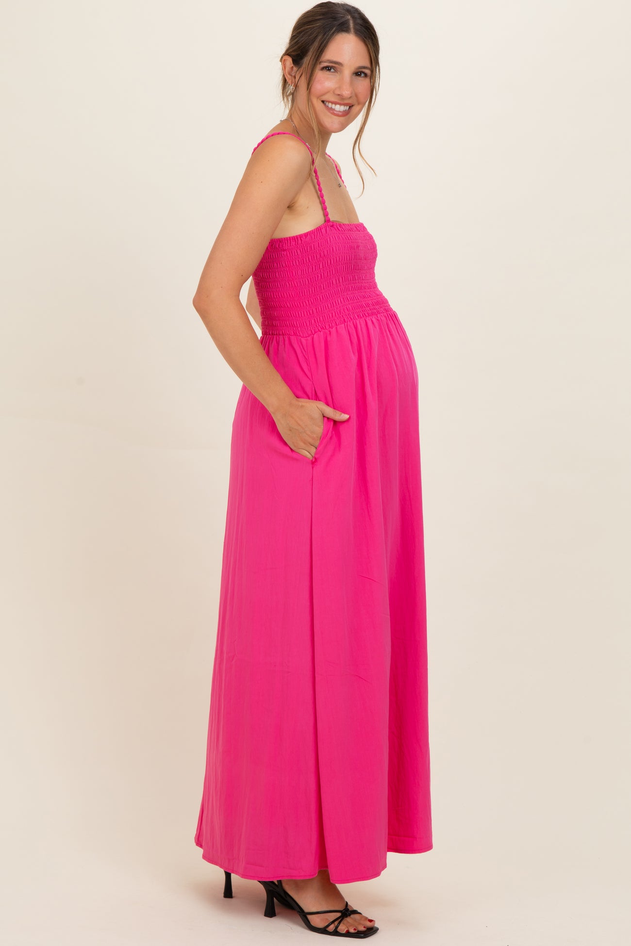 woman wearing a vibrant pink maternity maxi dress with a smocked bodice and pockets, showcasing a baby bump