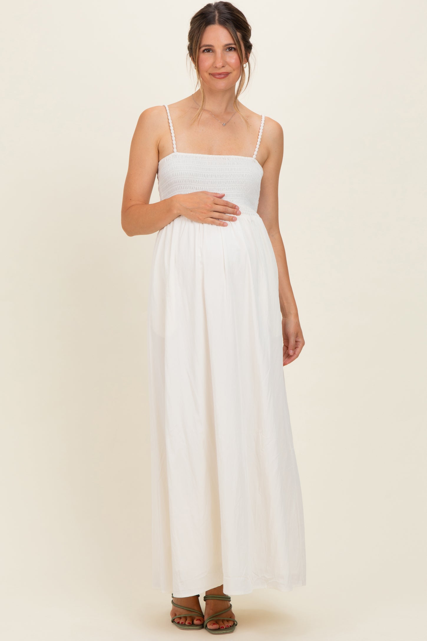 woman wearing a white maternity maxi dress with a smocked bodice and holding her baby bump
