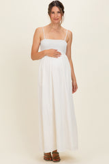 woman wearing a white maternity maxi dress with a smocked bodice and holding her baby bump