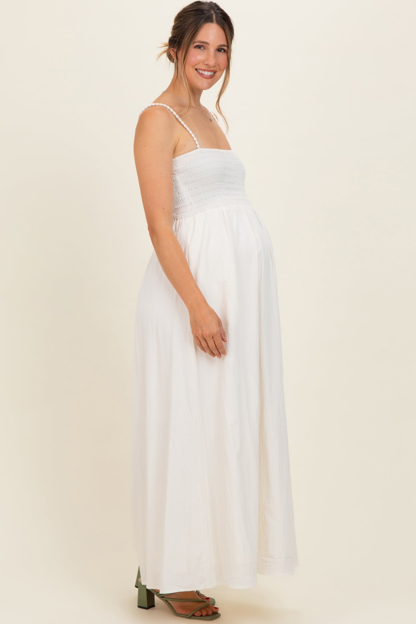 woman wearing a white sleeveless smocked maternity maxi dress and showing her baby bump