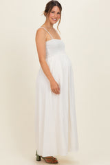 woman wearing a white sleeveless smocked maternity maxi dress and showing her baby bump