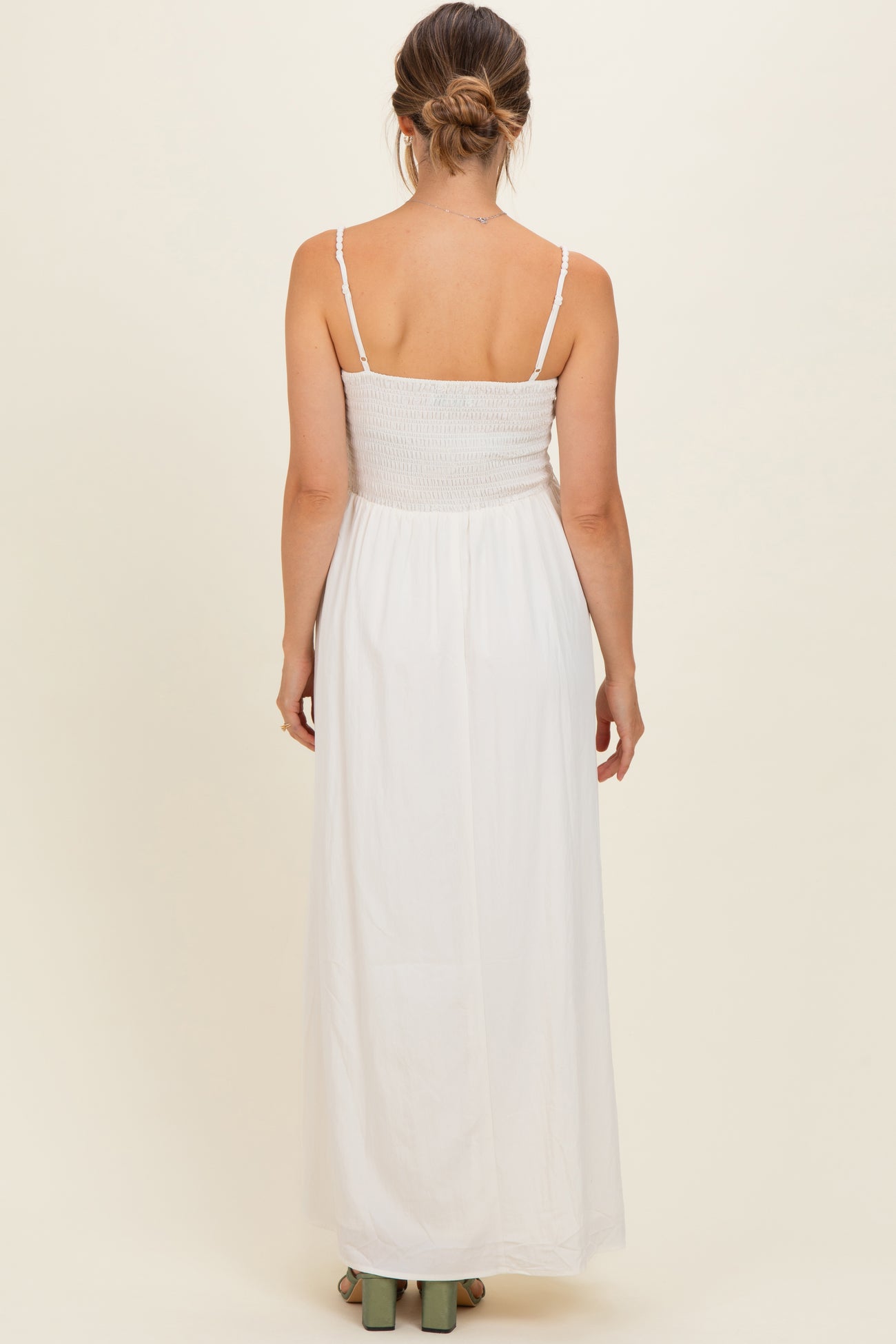 woman wearing a white maternity maxi dress with a smocked bodice and adjustable spaghetti straps, showing her back