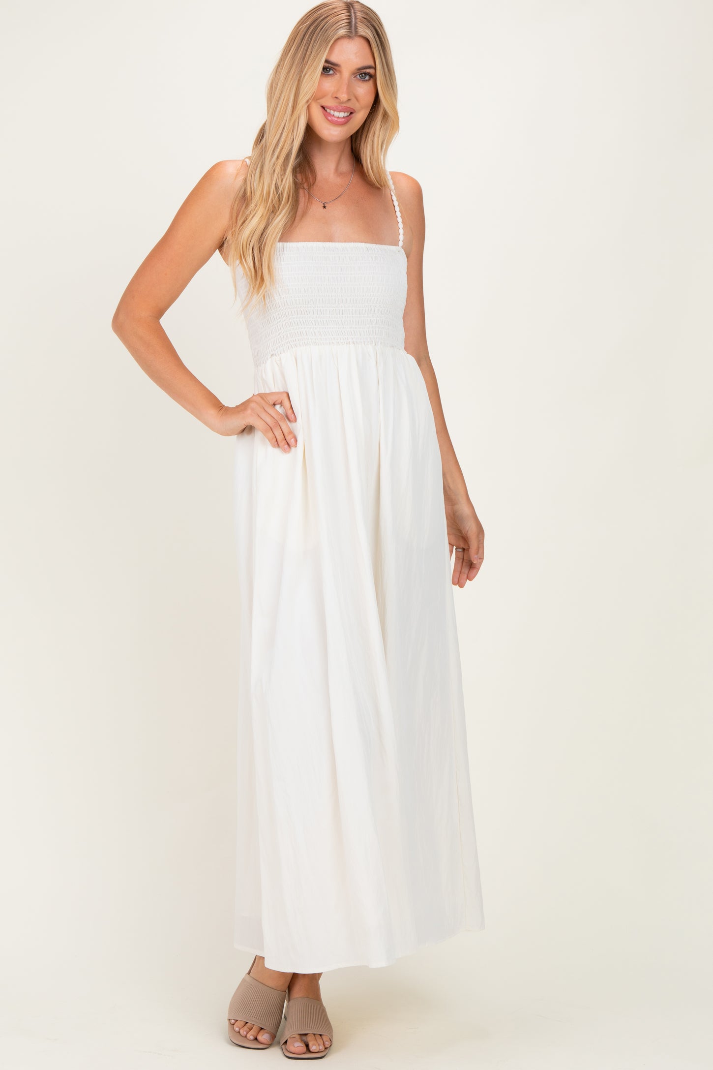 woman wearing a white maxi dress with a smocked bodice and adjustable straps, styled with beige slide sandals