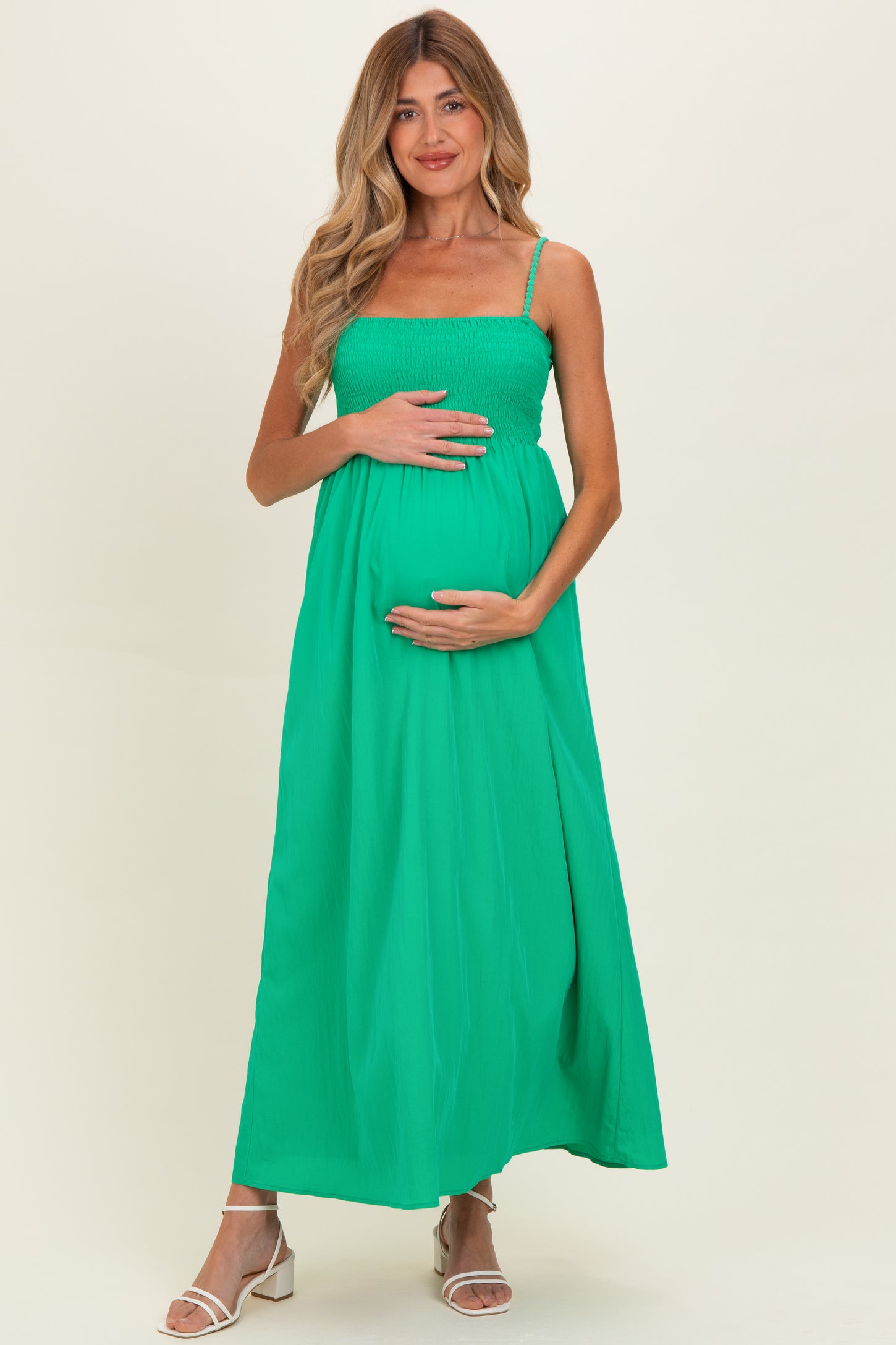 woman wearing a bright green maternity maxi dress with a smocked bodice, holding her baby bump