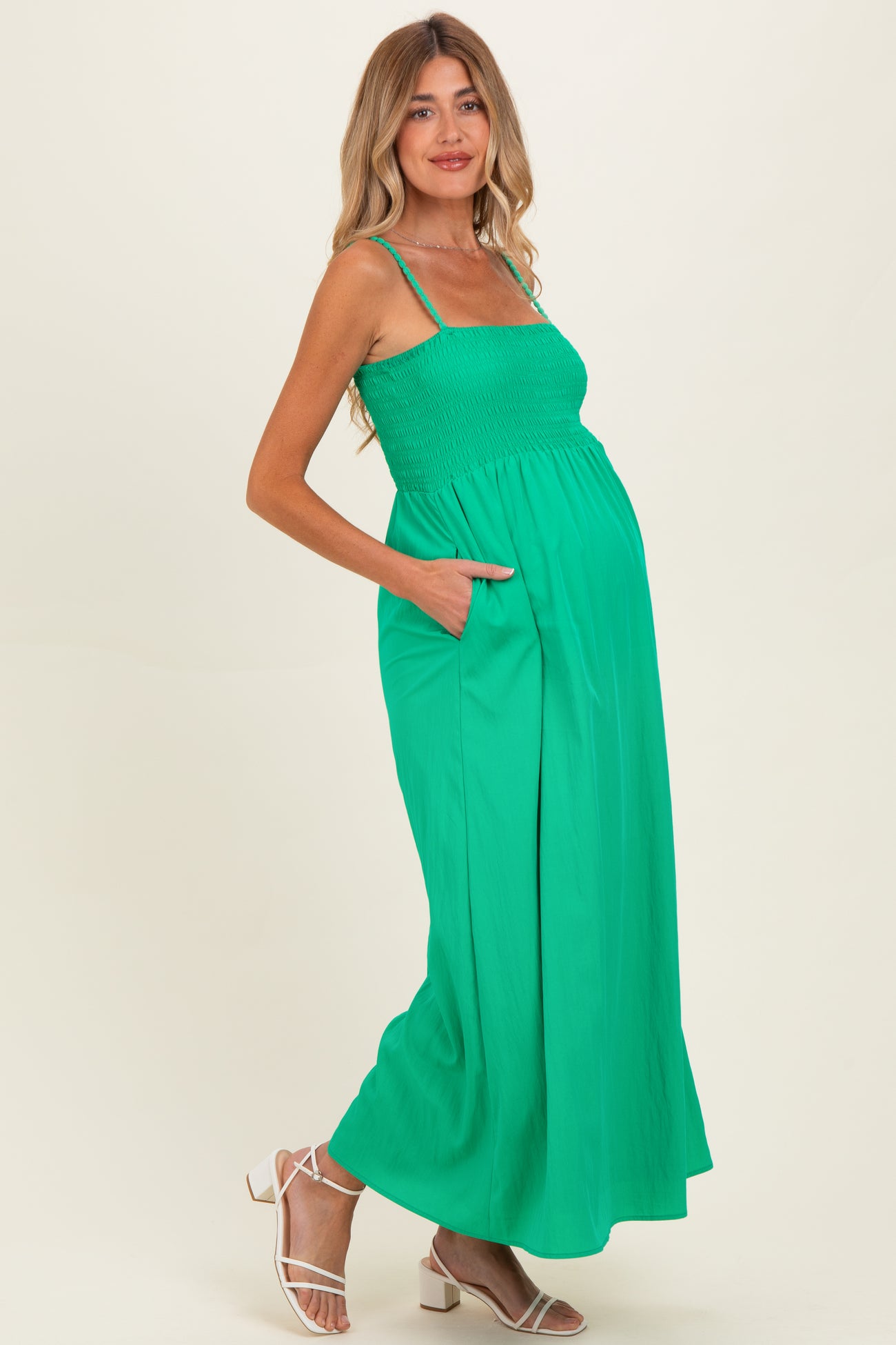 woman wearing a bright green maternity maxi dress with smocked bodice and pockets, showcasing her baby bump