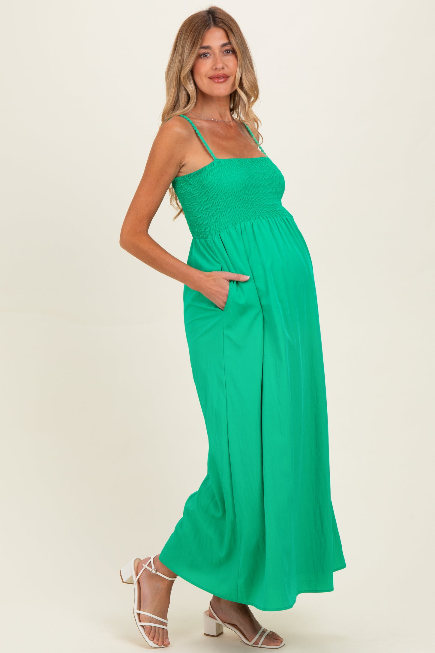 woman wearing a bright green maternity maxi dress with smocked bodice and pockets, showcasing her baby bump