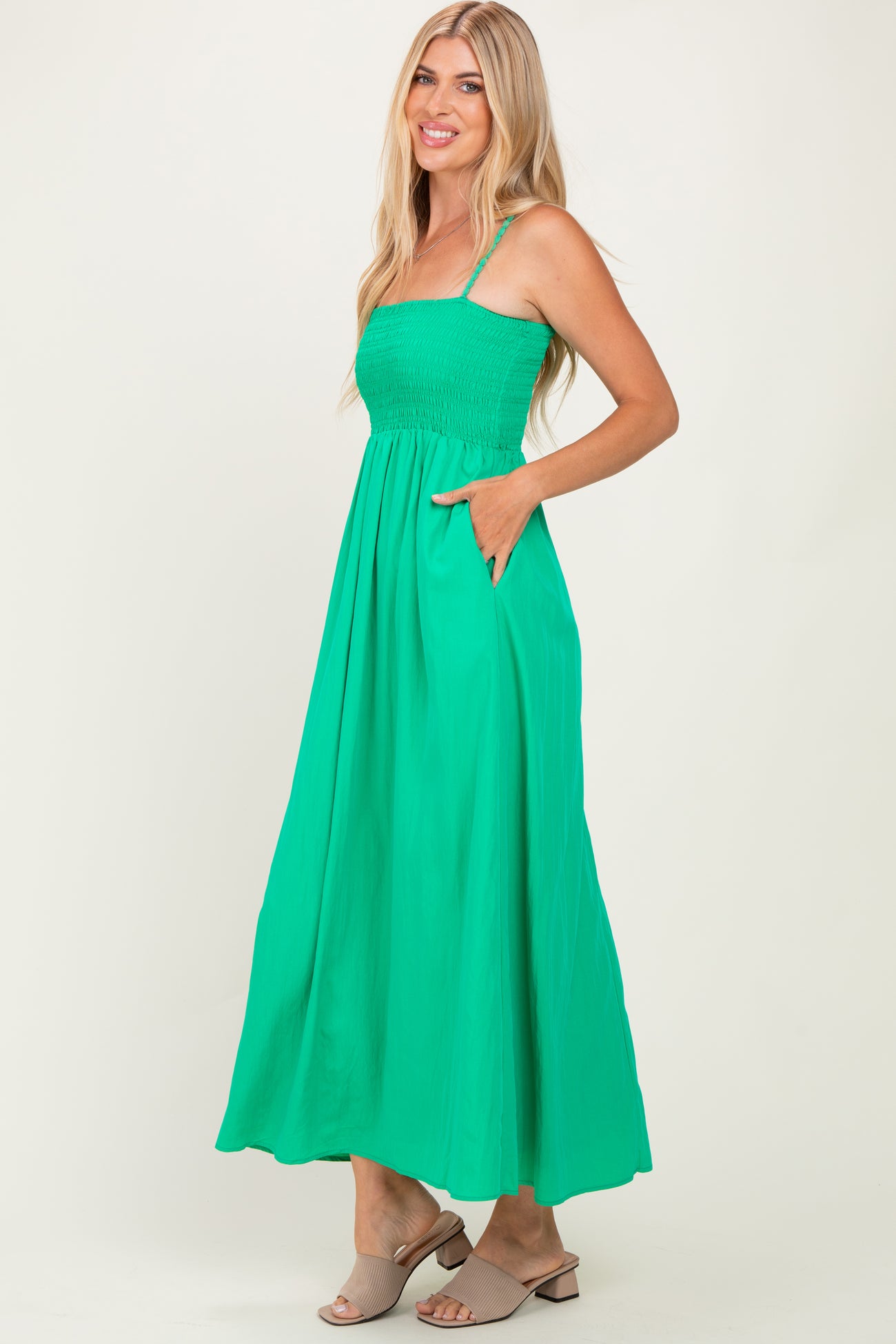 woman wearing a bright green maxi dress with a smocked bodice and pockets, standing sideways and smiling