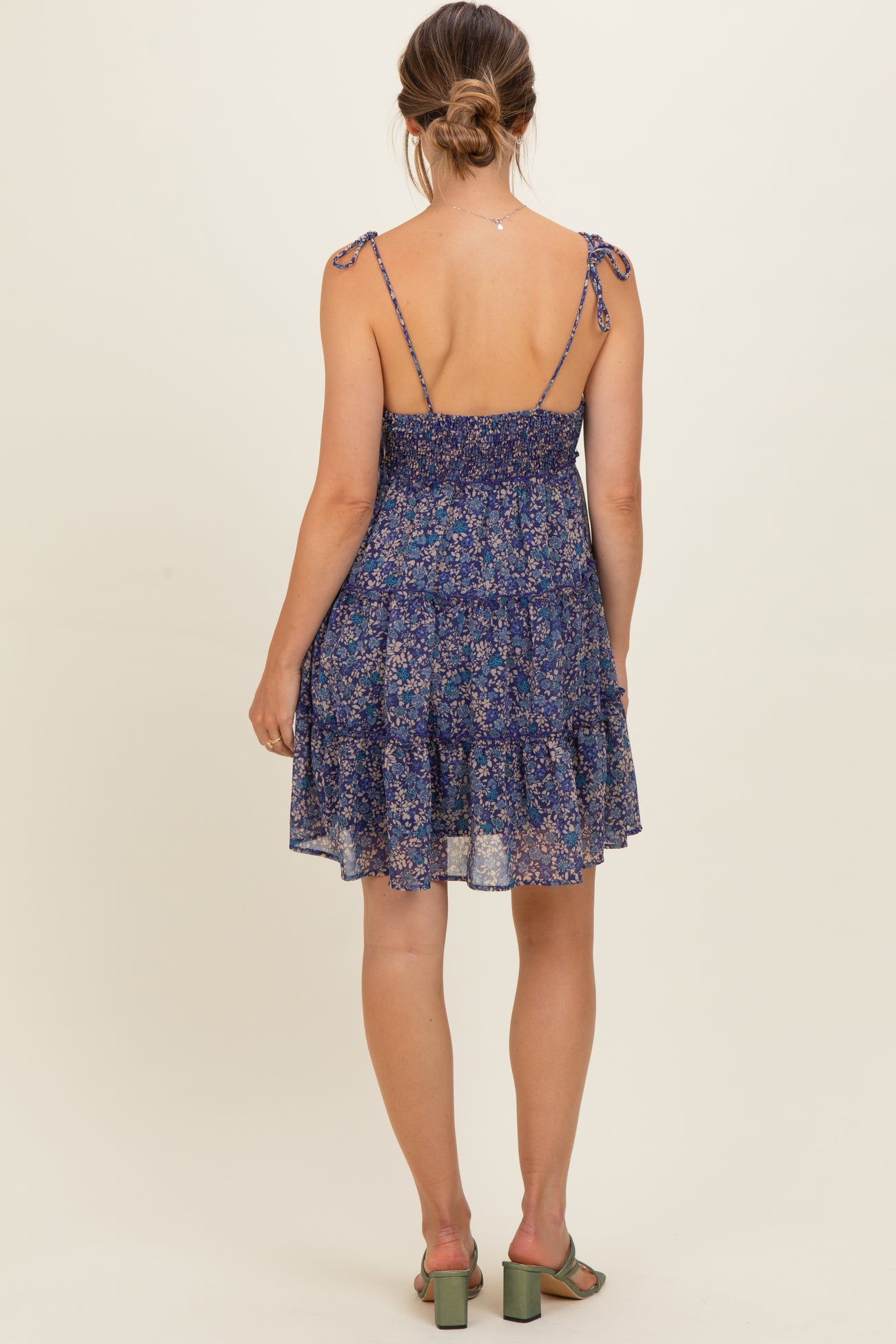 woman wearing a navy floral maternity dress with adjustable tie straps and a tiered skirt, showing a baby bump