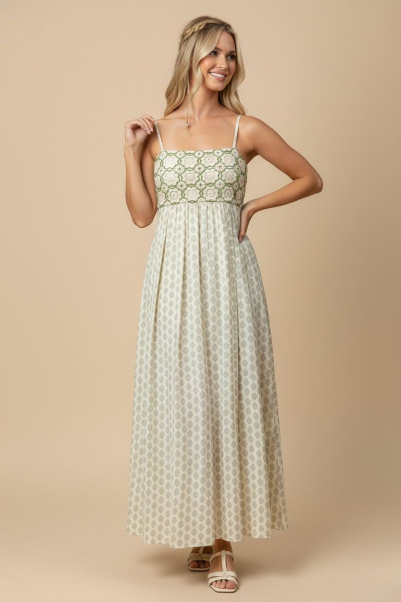 woman wearing a cream maxi dress with green geometric patterns and thin spaghetti straps