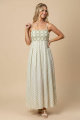 woman wearing a cream maxi dress with green geometric patterns and thin spaghetti straps