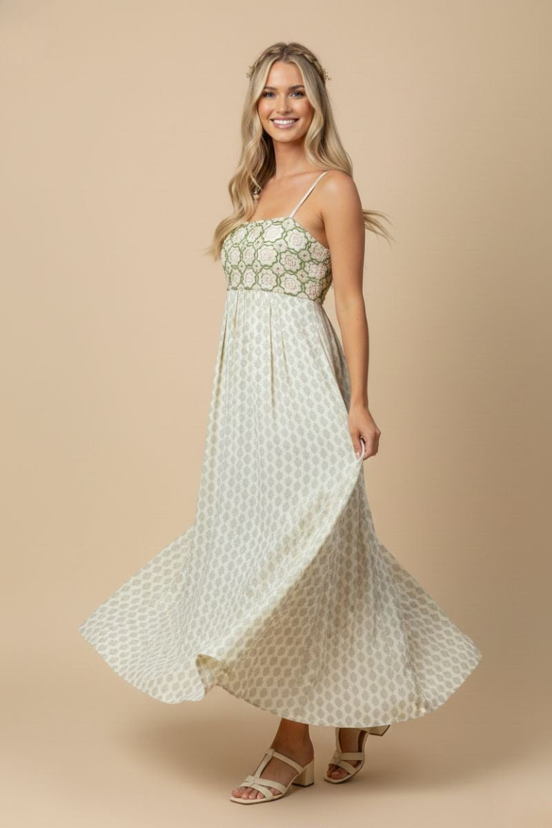 woman wearing a patterned maxi dress with a fitted bodice and flowing skirt, smiling and standing against a neutral background