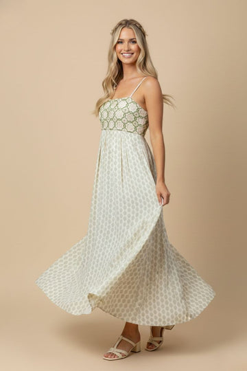 woman wearing a patterned maxi dress with a fitted bodice and flowing skirt, smiling and standing against a neutral background