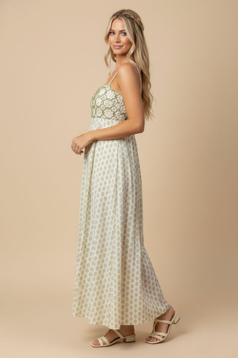 woman wearing a sleeveless maxi dress with a green and white floral pattern and strappy sandals
