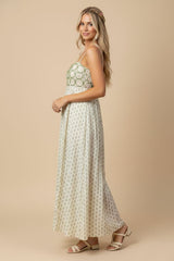 woman wearing a sleeveless maxi dress with a green and white floral pattern and strappy sandals