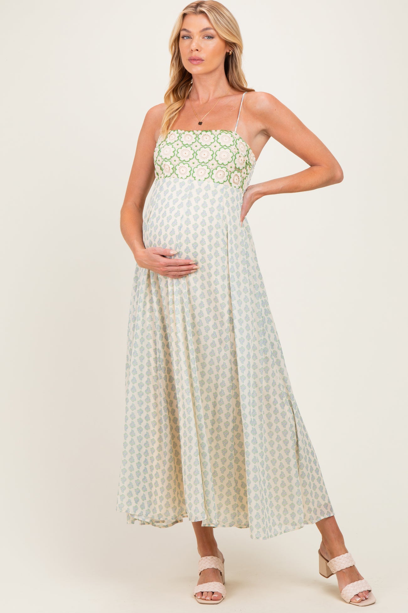 woman wearing a green and cream floral maternity maxi dress, holding her baby bump