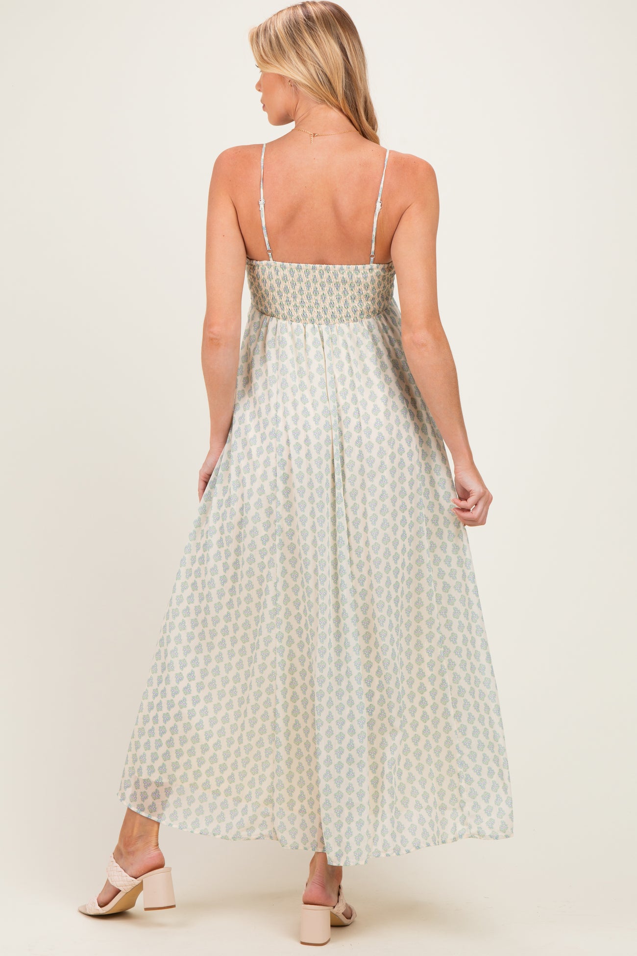 woman wearing a light green and cream patterned maternity maxi dress with adjustable straps, showing her back
