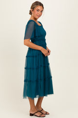 woman wearing a teal tiered tulle dress with short sleeves and a fitted bodice, styled with black sandals