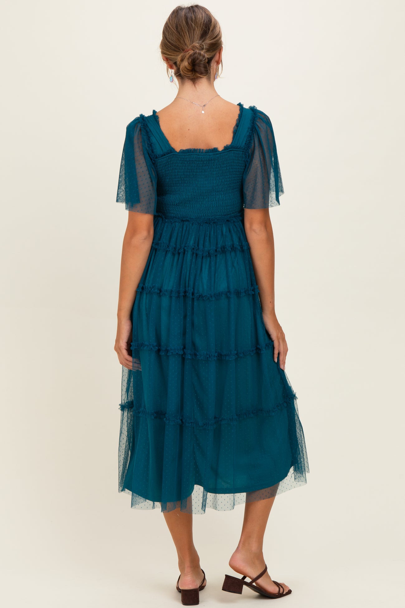 woman wearing a teal tiered midi dress with sheer short sleeves and a smocked bodice, viewed from the back