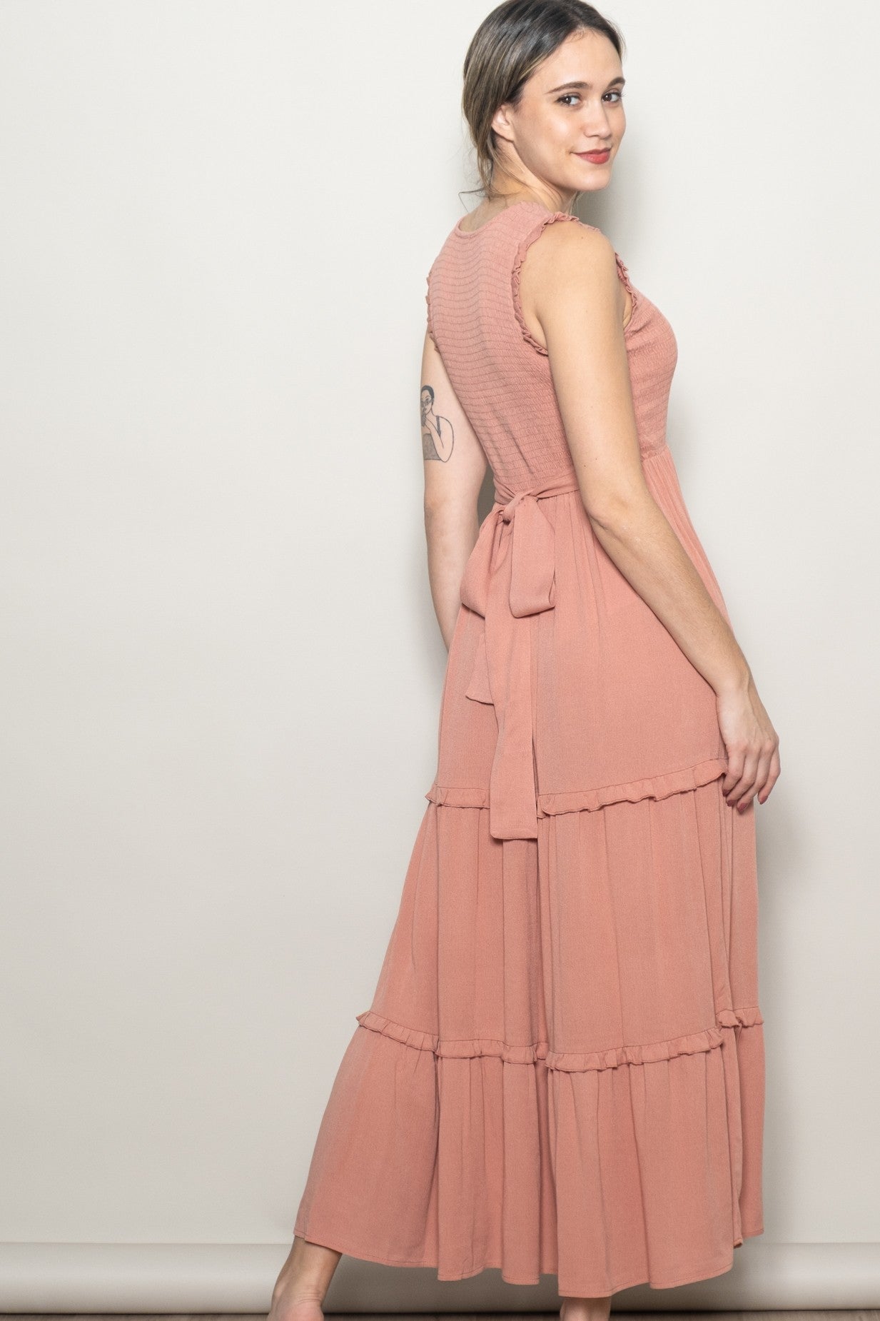 woman wearing a dusty rose tiered maxi dress with a tie waist and textured bodice, posing sideways against a neutral background