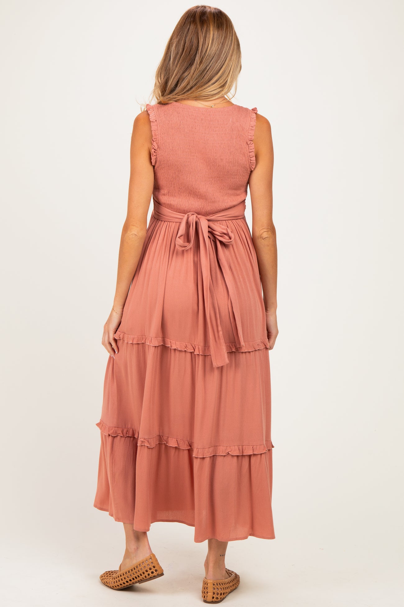 woman wearing a rust-colored maternity maxi dress with ruffle details and a tie back, viewed from the back