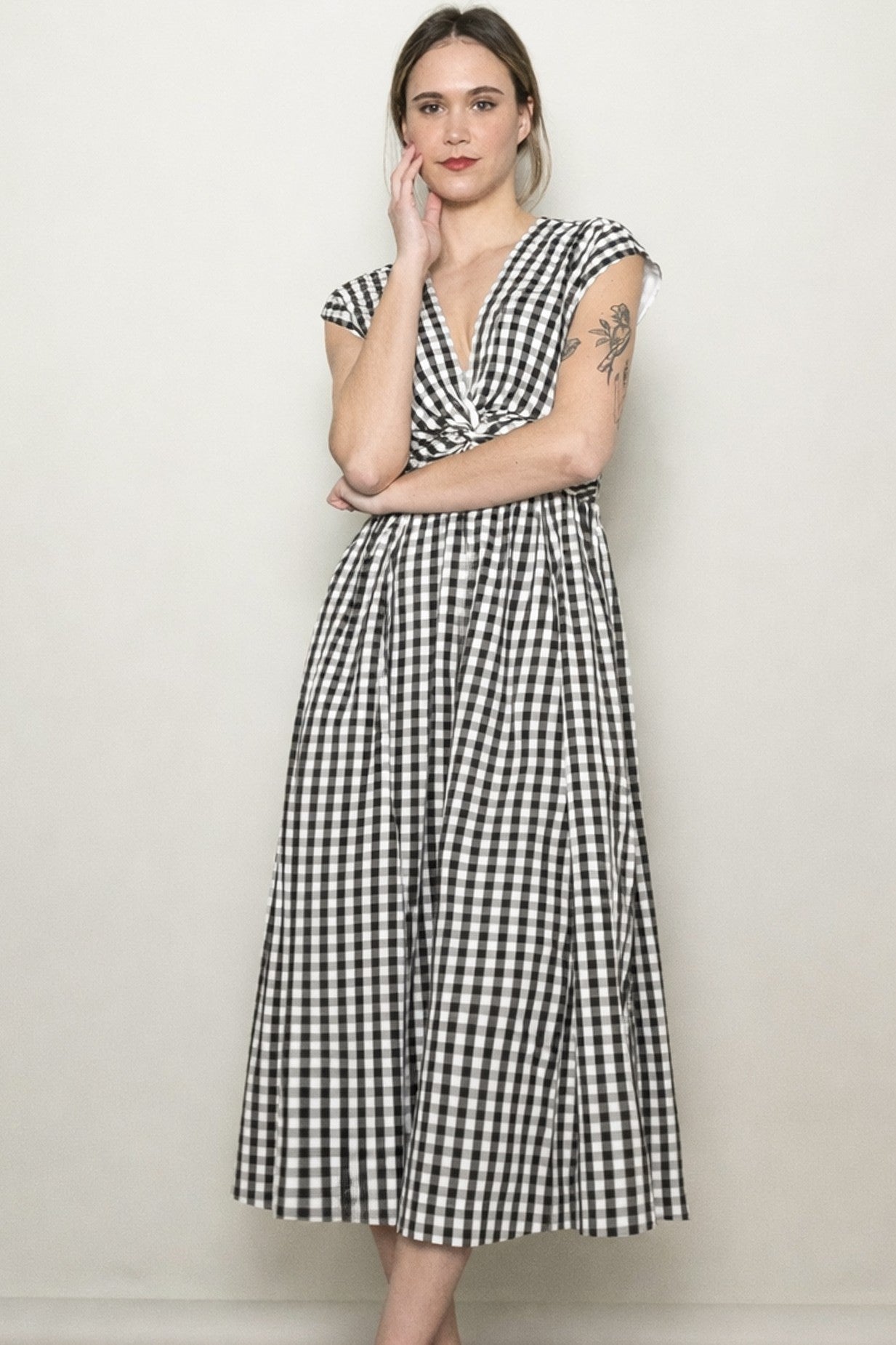 woman wearing a black and white gingham midi dress with cap sleeves and a cinched waist standing against a plain background