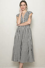 woman wearing a black and white gingham midi dress with cap sleeves and a cinched waist standing against a plain background