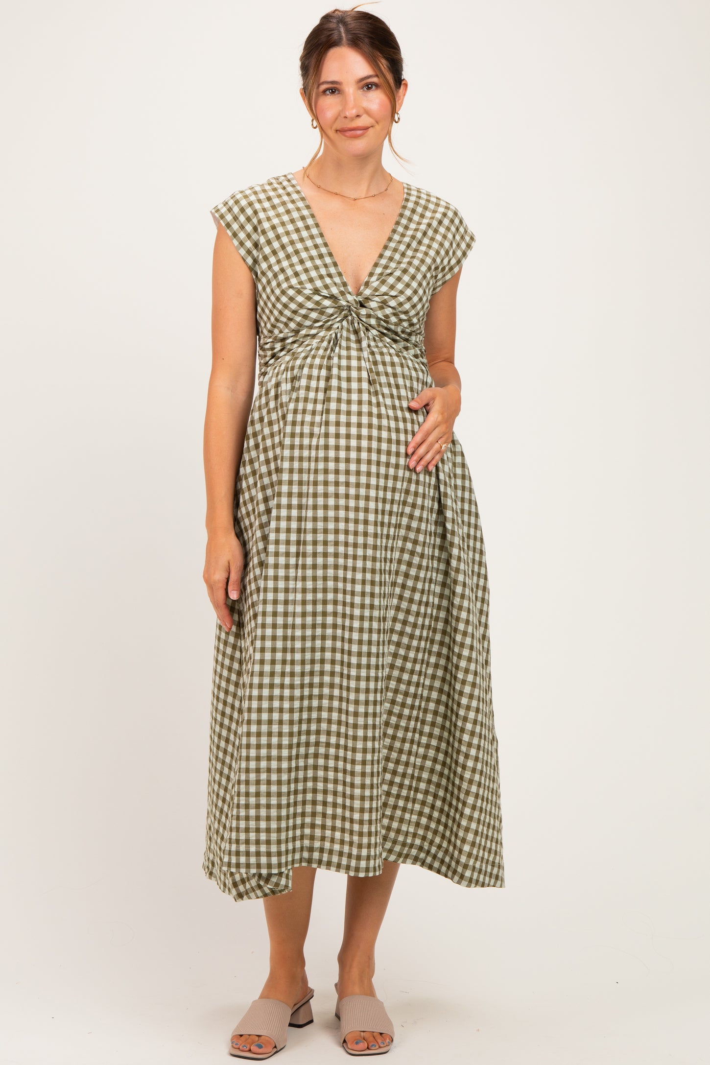 woman wearing a green and white gingham maternity dress with a knot detail at the front and holding her baby bump