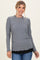 woman wearing a gray long sleeve top with a scalloped hem and black layering underneath, smiling against a light background