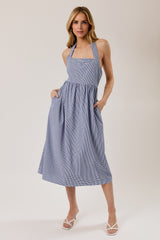 woman wearing a blue and white gingham halter neck midi dress with pockets
