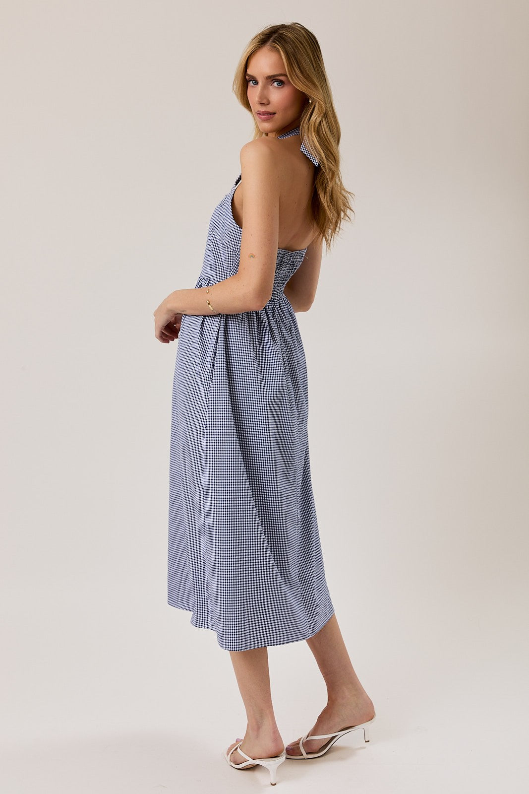 woman wearing a blue and white gingham halter neck mid-length dress, standing with her back to the camera