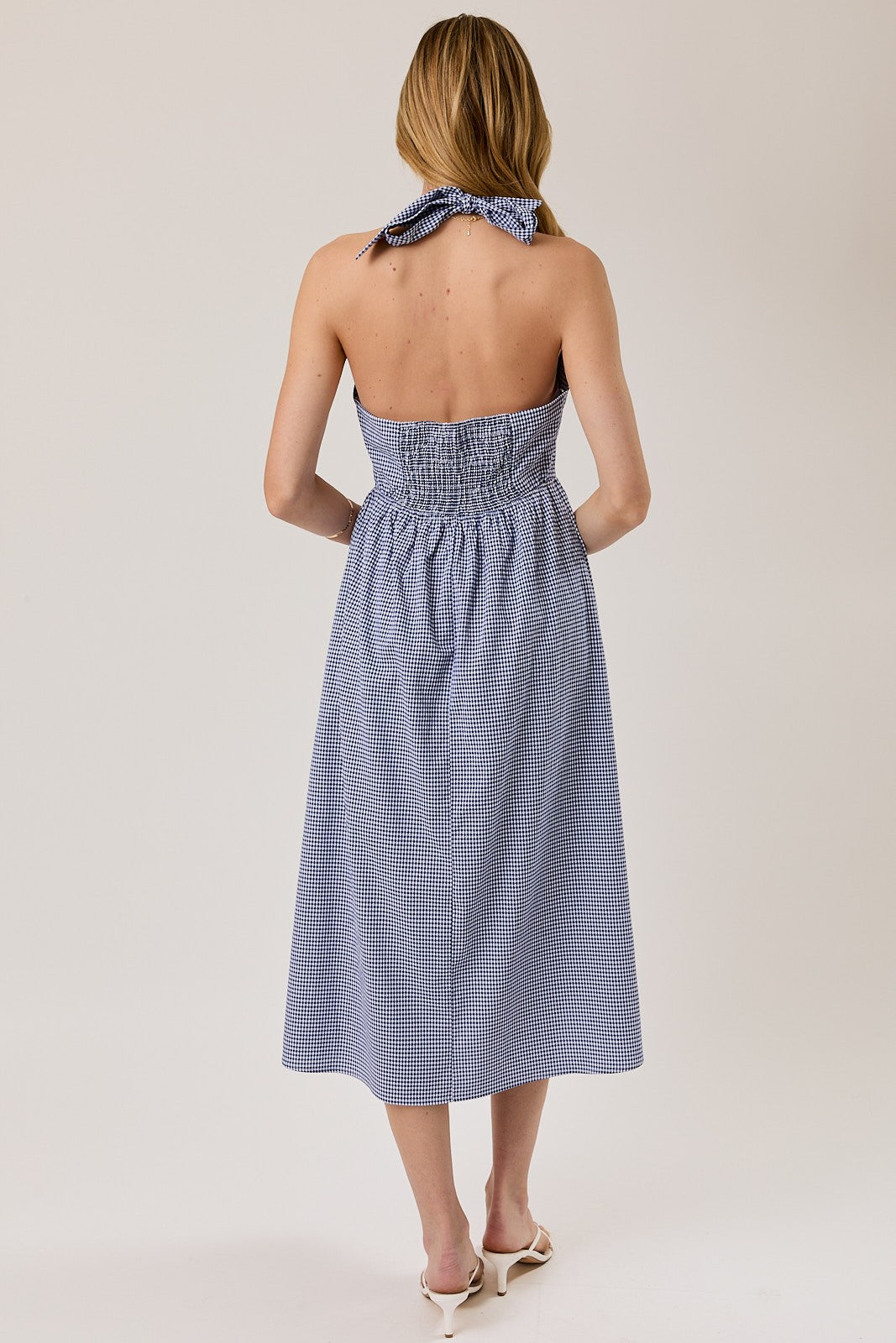 woman wearing a blue and white gingham strapless dress with a tie back and smocked bodice, showing the back view