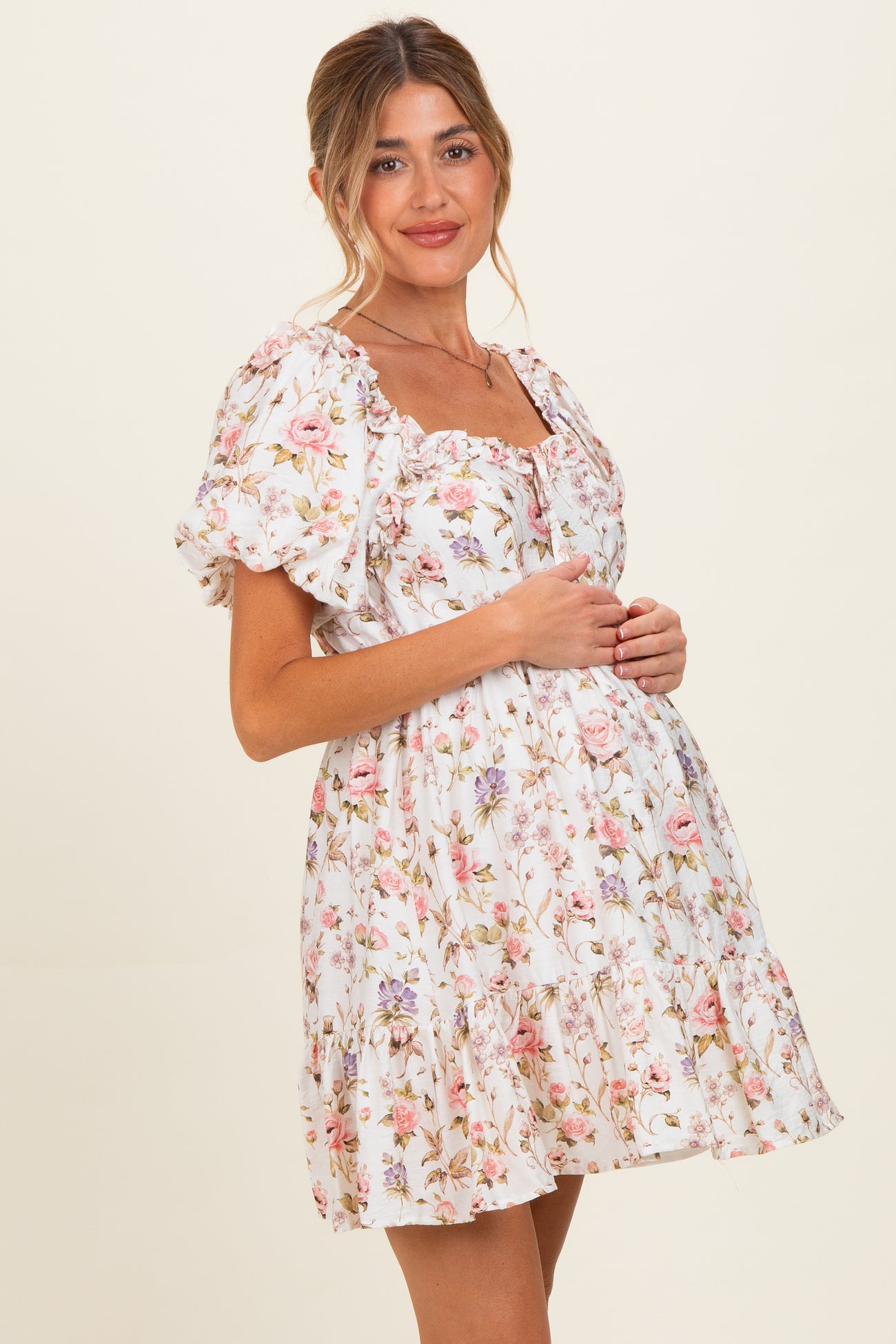 woman wearing a white floral maternity dress with puff sleeves and a gathered waist, showing her baby bump