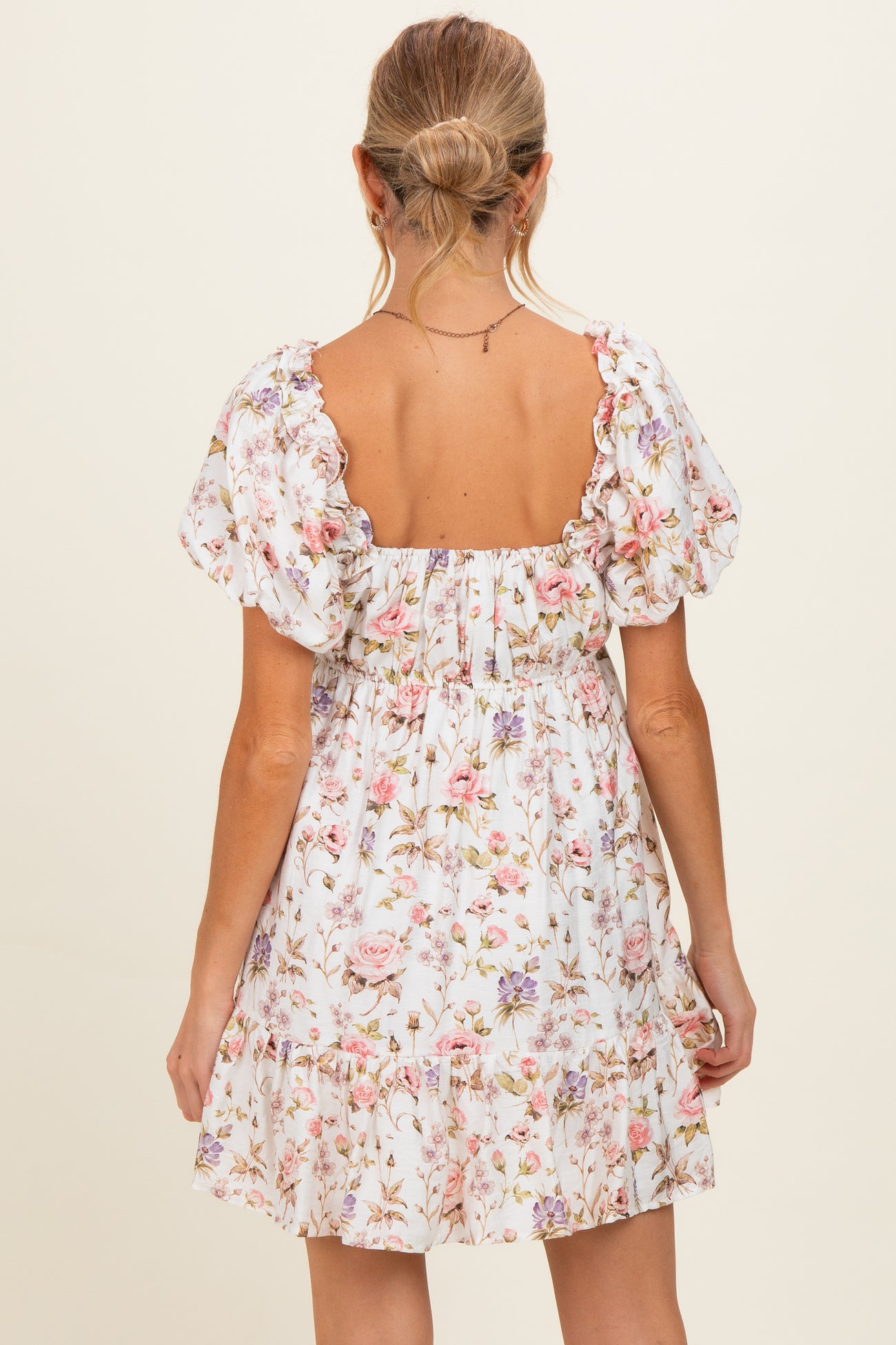 woman wearing a floral print maternity dress with puff sleeves and a tiered hem, showing a bare back