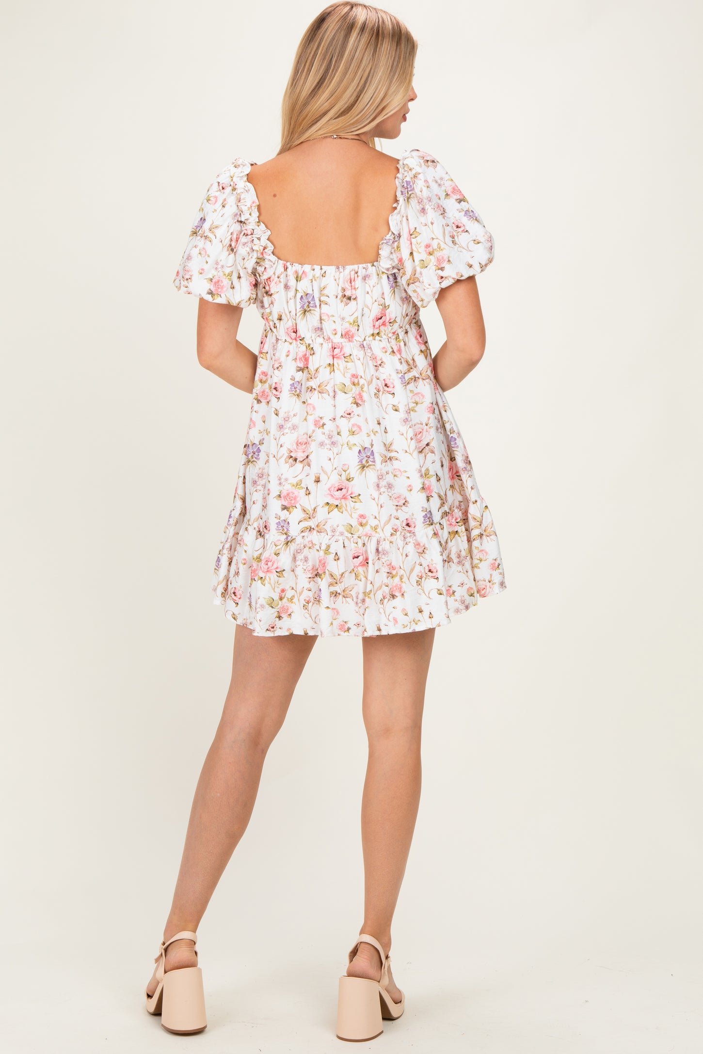 woman wearing a white floral print short dress with puff sleeves and a backless design