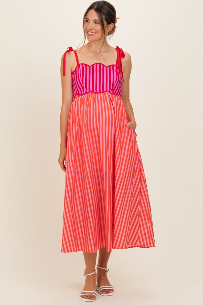 woman wearing a pink and red striped maternity dress with a scalloped neckline and tie straps, shows baby bump