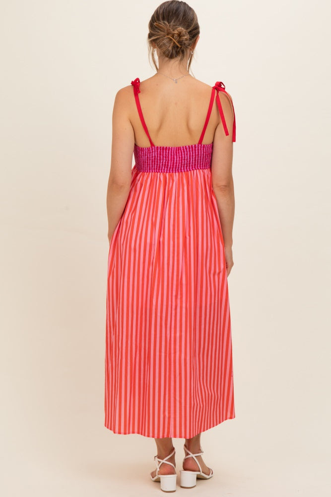 woman wearing a pink and orange striped maternity maxi dress with tie straps and a smocked bodice, showing her back