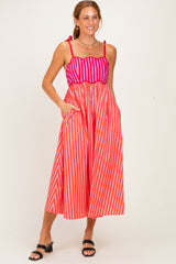 woman wearing a pink and red striped maxi dress with pockets and tie straps, smiling against a light background