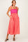 woman wearing a pink and red striped maxi dress with pockets and tie straps, smiling against a light background