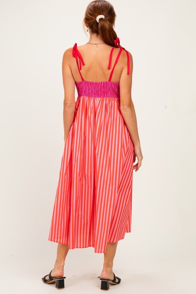 woman wearing a back view of a pink and orange striped maxi dress with a smocked bodice and adjustable straps