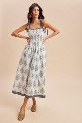 woman wearing a white floral maxi dress with smocked bodice and tie straps, standing with one hand on her hip