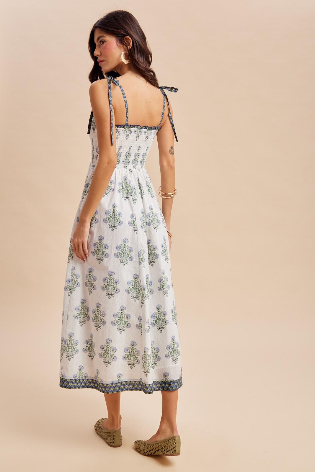woman wearing a white tie-back sundress with green and blue floral patterns, showing a relaxed fit and midi length