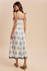 woman wearing a white tie-back sundress with green and blue floral patterns, showing a relaxed fit and midi length