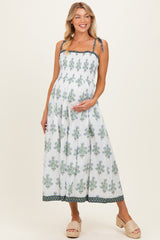 woman wearing a white maternity maxi dress with floral print and tie straps, gently holding her baby bump